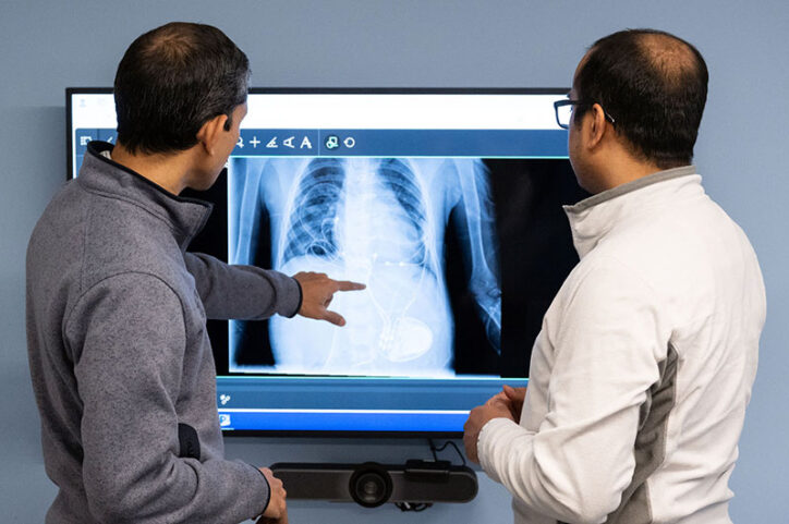 A doctor points at a pacemaker shown in an X-ray, while a doctor to his right looks at the screen.