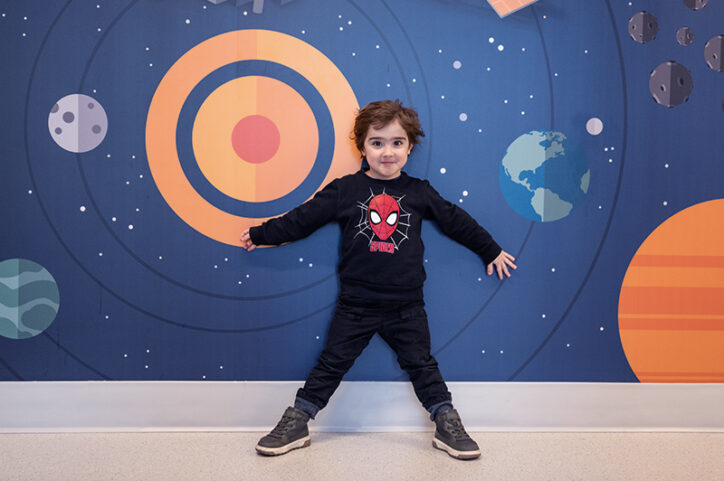 Lucas, who has duchenne muscular dystrophy, poses in front of a mural of a galaxy