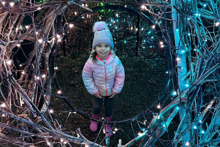 Teagan, who has hearing loss, smiles through a circle of Christmas lights outside.