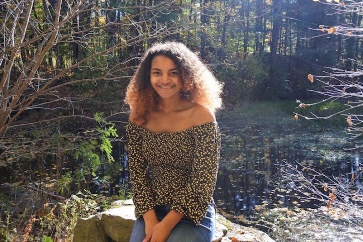 Atiana sits on a boulder in a wooded area.