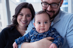 A woman smiling next to a man holding a baby.