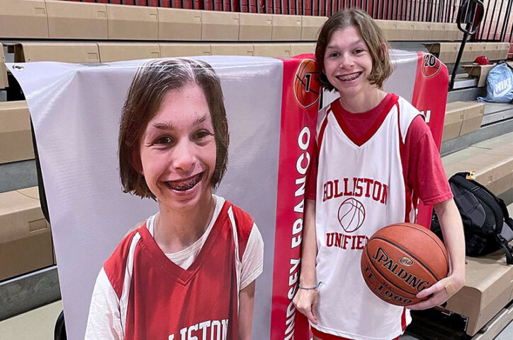 Lindsey, holding a basketball in her left arm, poses in front a large poster that features a photo of her.