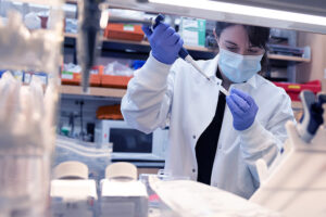 A masked researcher at the lab bench pipetting, to illustrate idea of genome sequencing.
