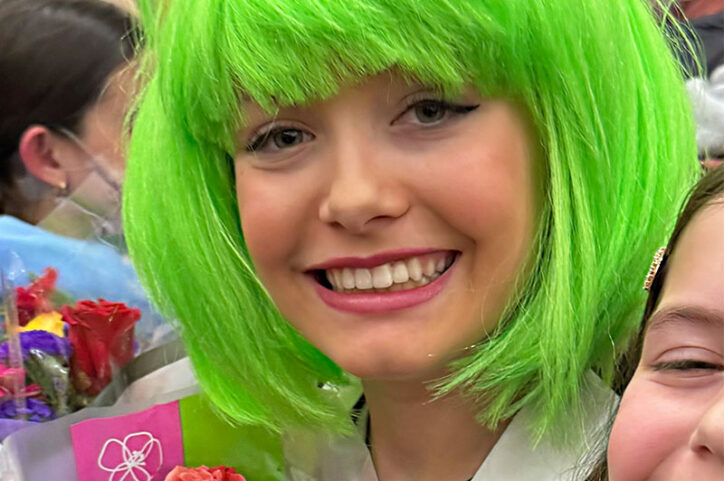 Lily smiles at the camera wearing a green wig and her teeth are straight without braces.