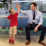 Four-year-old Jack stands on his tippy toes to high-five his cardiologist, who is seated.