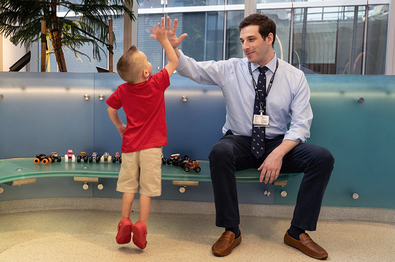 Four-year-old Jack stands on his tippy toes to high-five his cardiologist, who is seated.