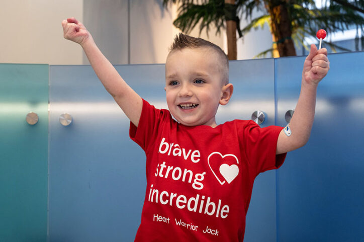 Jack lifts his arms in the air as a gesture of happiness, while holding to a lollipop. 