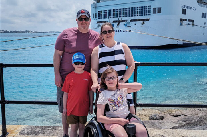 Sydney in her wheelchair with her parents and brother in front of a cruise ship