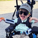 Maxwell smiles and laughs in his wheelchair