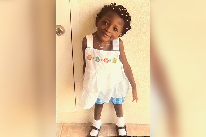 Thelma smiling in an embroidered summer top. Due to congenital scoliosis, her head tilts to the left.