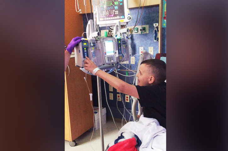 A boy hooked up to an IV infusion in his hospital bed, pressing a button.