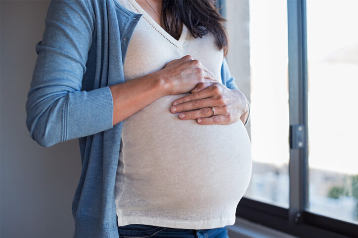 A pregnant women holding her belly by a window.