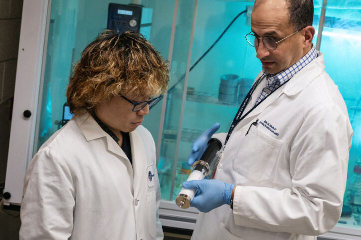 A doctor, on right, holds a large syringe containing microbubbles while talking to his research colleague.