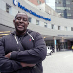 A smiling Branden Baptiste in front of the Boston Children’s Hospital entrance, after his base editing treatment.