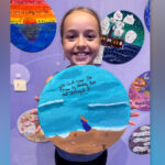 Kathryn poses with her painted tile, which reads, “You can’t cross the ocean by standing there and staring at it.”