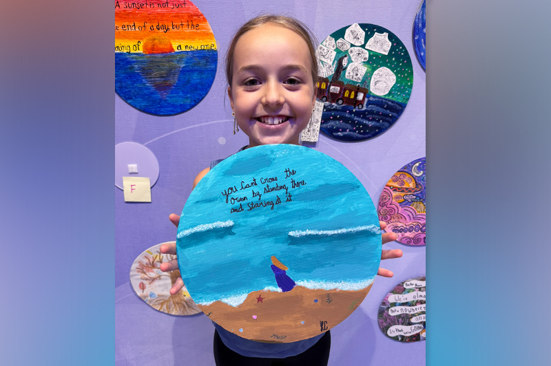 Kathryn poses with her painted tile, which reads, “You can’t cross the ocean by standing there and staring at it.”