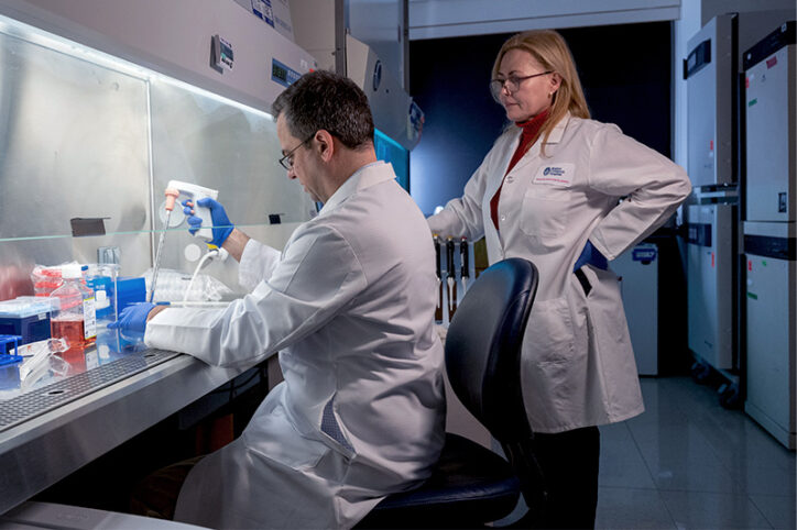 Researchers feed cultured lung cells in a lab room.