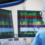 A cardiologist looks at two monitors that show electrical signals indicating the spot of conduction tissue.