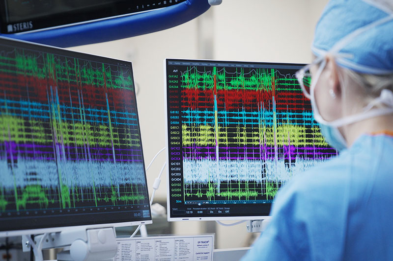 A cardiologist looks at two monitors that show electrical signals indicating the spot of conduction tissue.