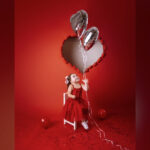 Everly looks up at heart-shaped balloons in front of a red backdrop.