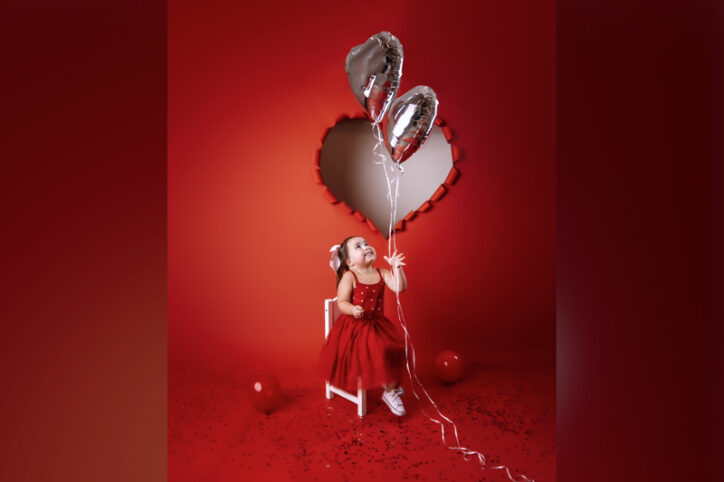 Everly looks up at heart-shaped balloons in front of a red backdrop.