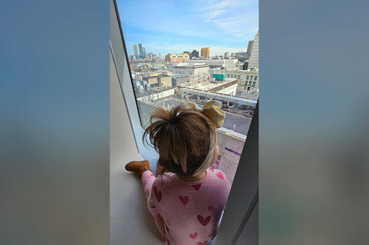 Everly sits on an interior window ledge while looking out at the city of Boston.