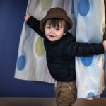 2-year-old boy who had brachial plexus birth injury peers out of a curtain in a medical exam room.