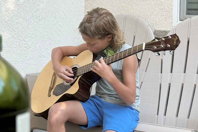 A boy concentrates on his guitar fingering.