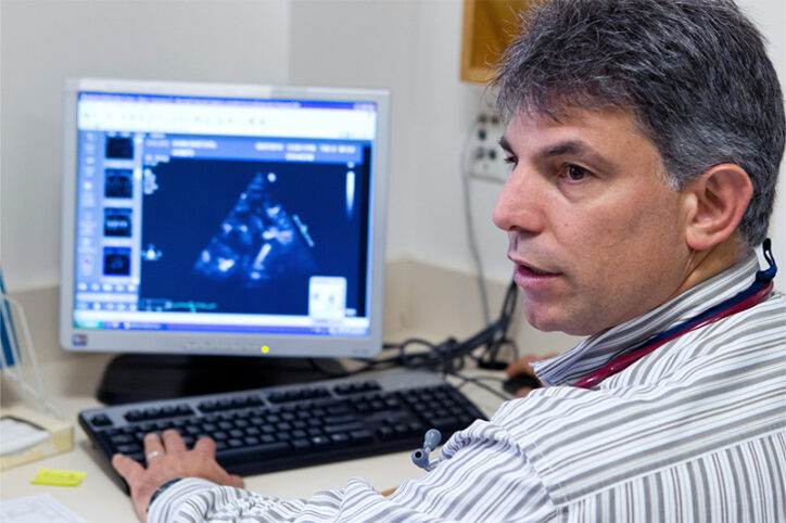 A doctor looks away from a computer screen that shows an image taken from an echocardiogram.