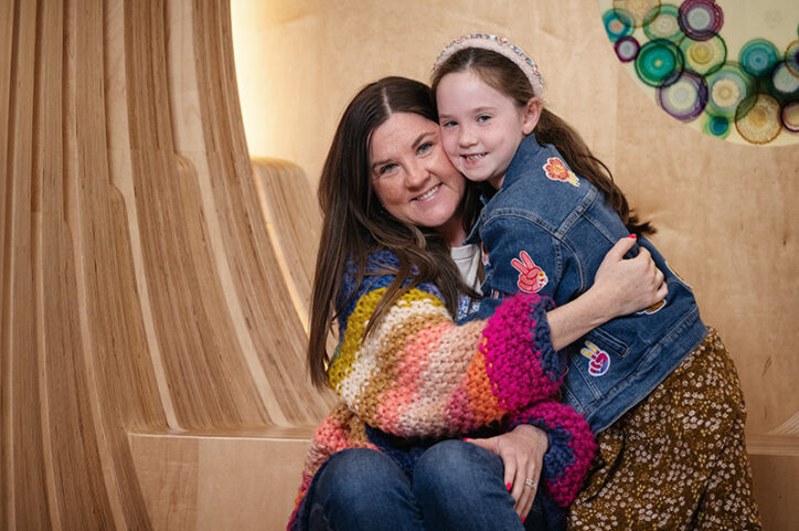 A six-year-old girl smiles as she hugs her mother inside a room at Boston Children's Hospital.