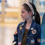 A 6-year-old wearing a jean jacket stands in a hospital hallway, gazing into the distance