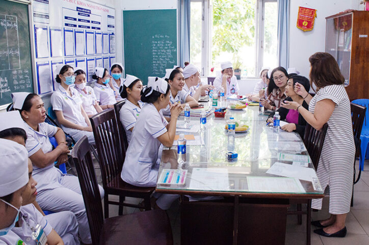 A group of nurses listen to a nurse educator presenting in a classroom.
