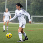 A young woman on an outdoor field gets ready to pass a soccer ball.