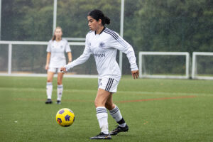 A young woman on an outdoor field gets ready to pass a soccer ball.