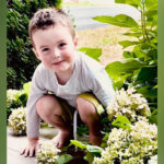 A young boy squatting on a porch.