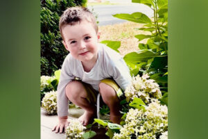 A young boy squatting on a porch.