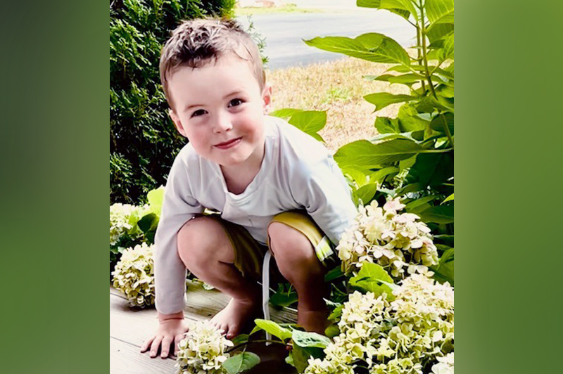 A young boy squatting on a porch.