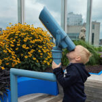 A young boy looks through a telescope set on a hospital rooftop.