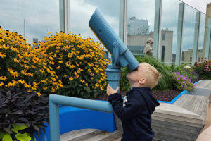 A young boy looks through a telescope set on a hospital rooftop.