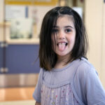 a dark-haired 5-year-old girl smiles while sticking out her tongue