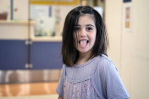 a dark-haired 5-year-old girl smiles while sticking out her tongue