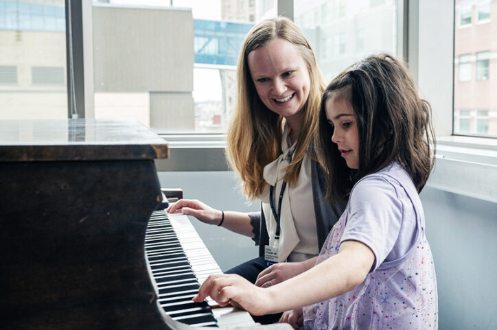 A dark-haired 5-year-old girl plays the piano with her female doctor