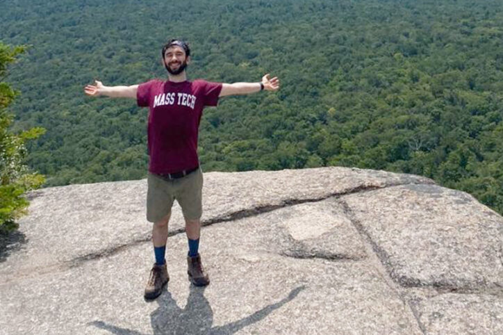 Stephan outstretches his arms horizontally and smiles while standing on a mountaintop.