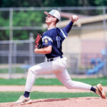 A teen baseball pitcher winds up on the mound during a game.