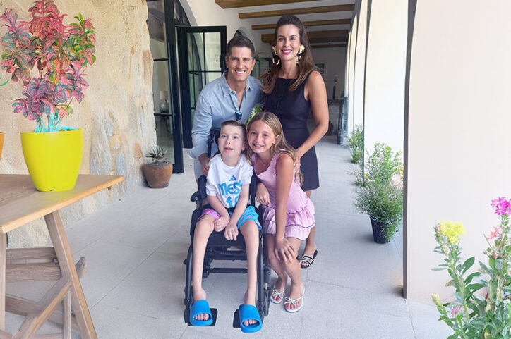 A father, mother, daughter, and son who is in a wheelchair, smiling together, surrounded by potted plants.