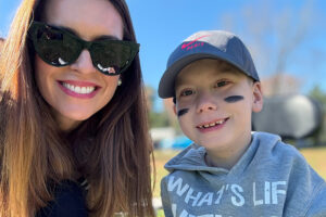 A mother and her son smiling at an outdoor sports event.