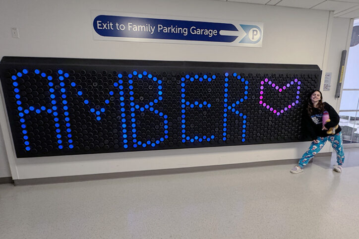 A young girl smiles next to a light-up board that says "Amber" with a heart.