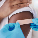 two gloved hands applying a bandaid to a child's upper arm
