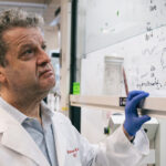 A male researcher examines mathematical models on a whiteboard.