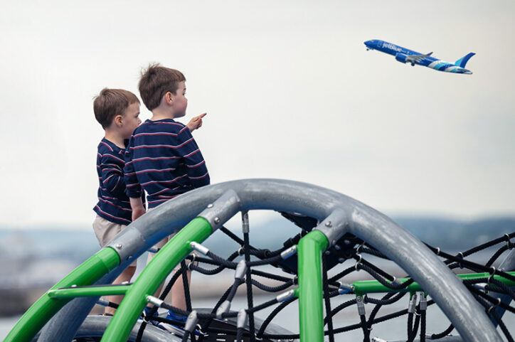 Two young boys watch a JetBlue plane take off in the distance